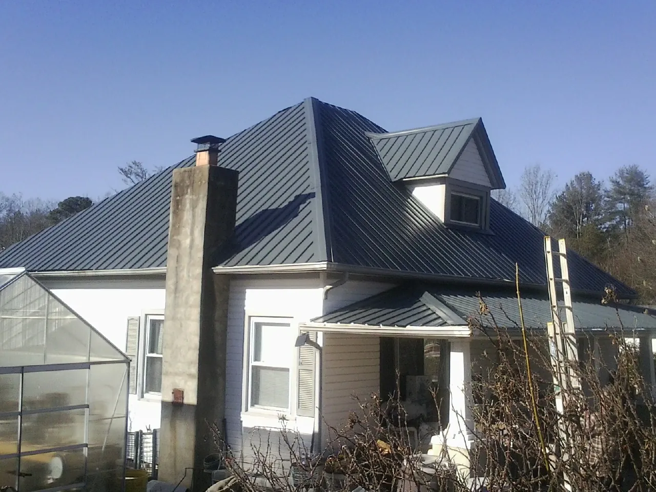 Dark blue standing seam metal roof on a white farmhouse with dormer — Slate & Tile Roof Repair by Roofing Brothers in Lake Peekskill