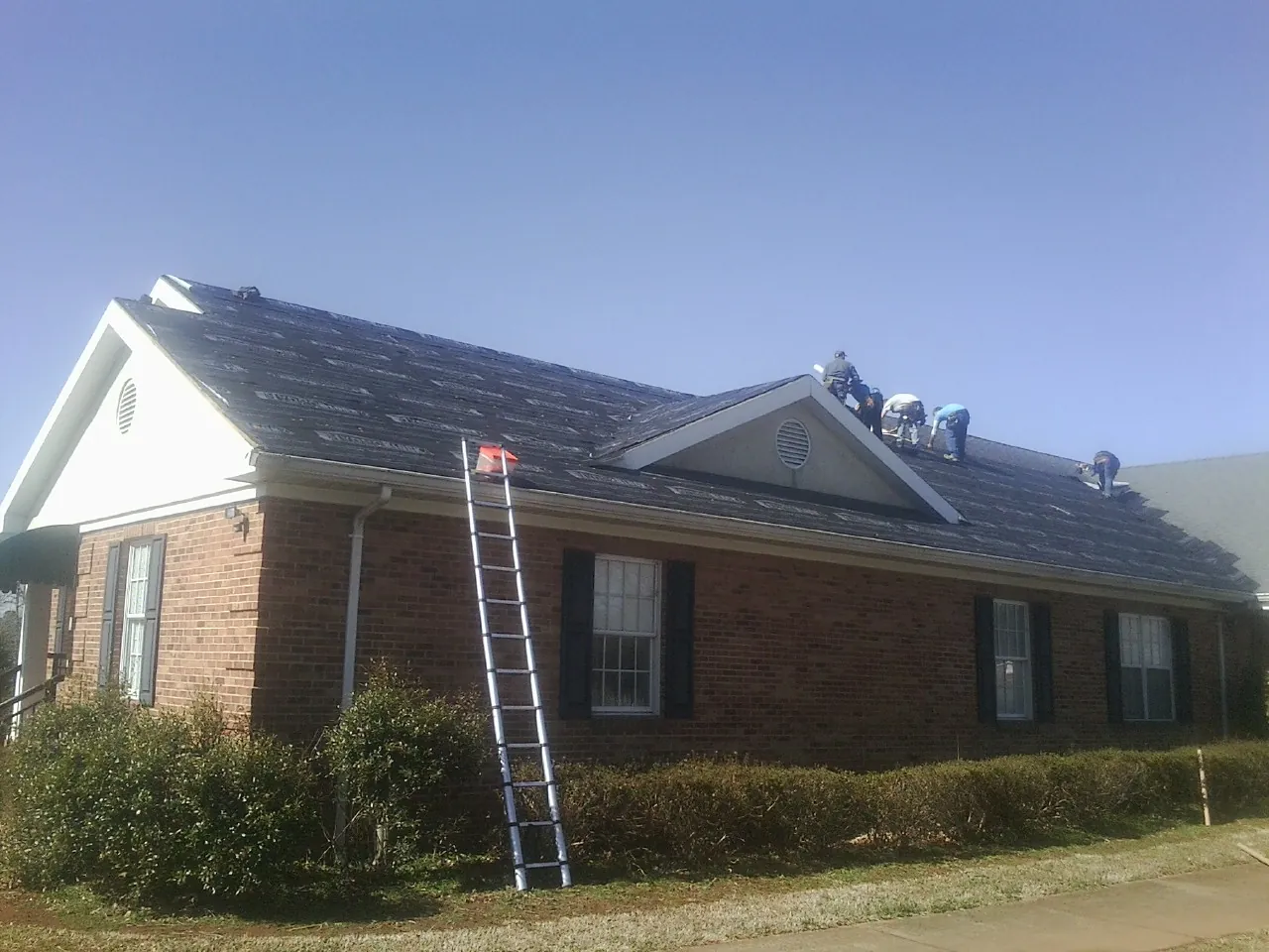 Crew tearing shingles off a brick ranch roof with a ladder set — Emergency Roof Repair work by our crew in Lake Peekskill