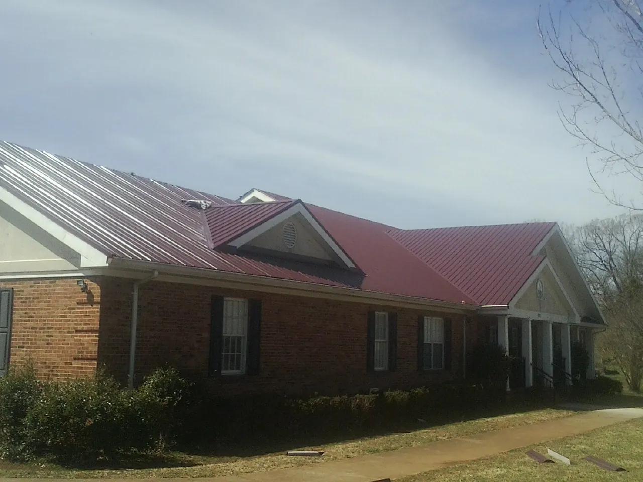 Red metal roof with gabled entries on a long brick building, from a Hail Damage Roof Repair job in Lake Peekskill
