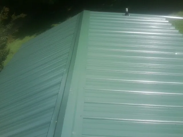 New green metal panels meeting at the ridge of a roof — Flat Roof Repair work by our crew in Lake Peekskill