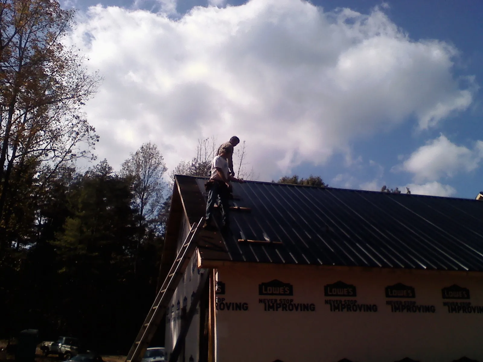 Roofer fastening dark metal panels high against a cloudy sky, from a Roof Inspection job in Lake Peekskill