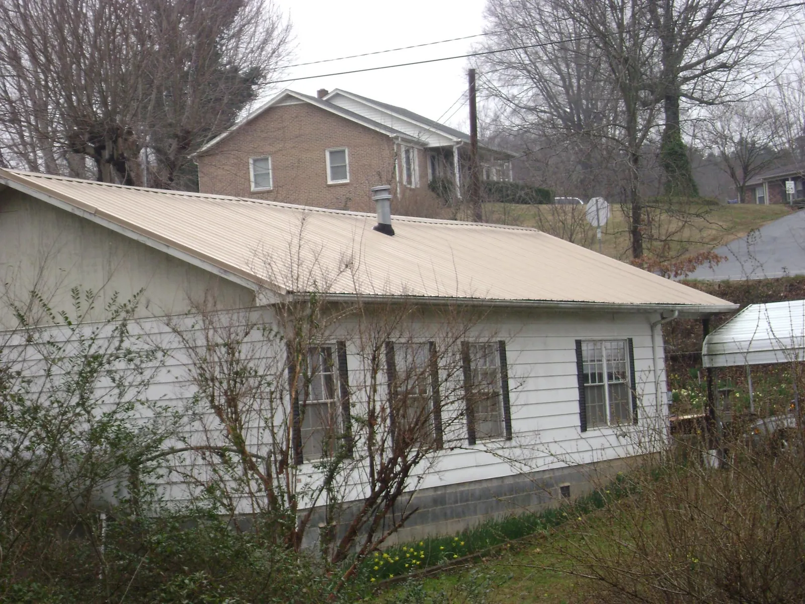 Tan metal roof on a white sided house set into a hillside — Commercial Roofing by Roofing Brothers in Lake Peekskill